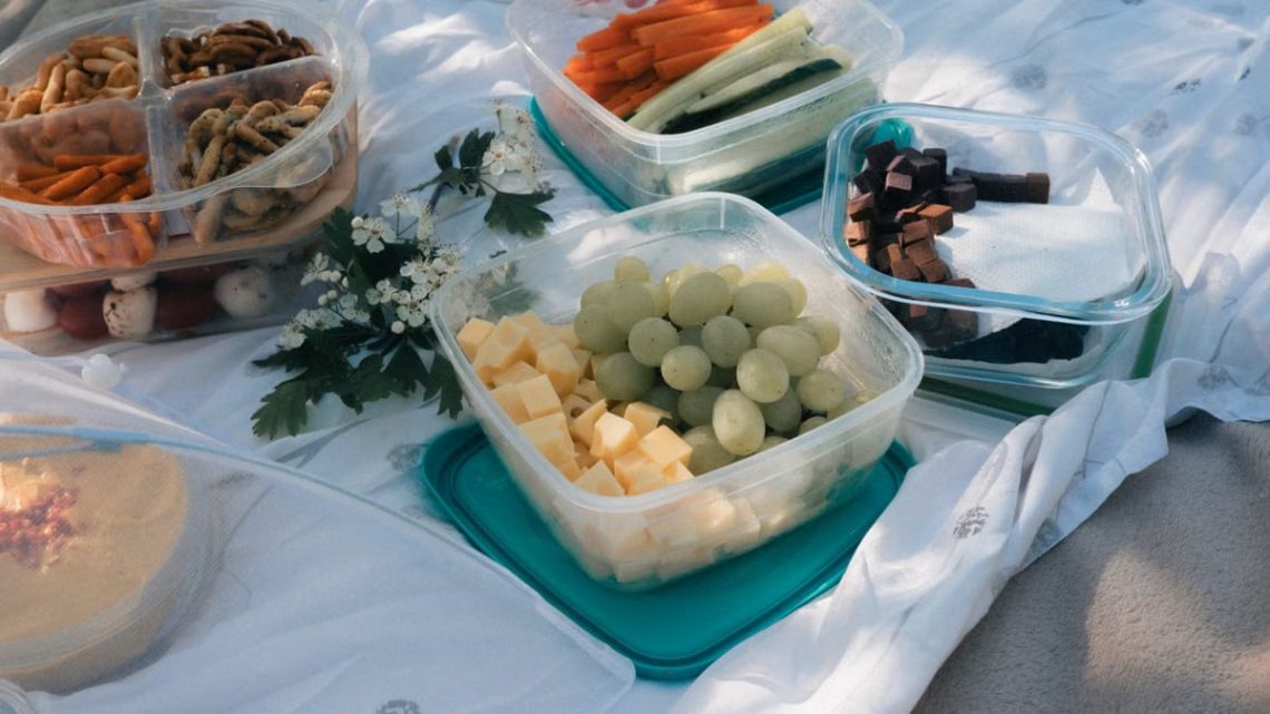 Picnic setup with containers of fruits, vegetables, and snacks arranged on a blanket, ideal for summer outings.
