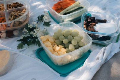 Picnic setup with containers of fruits, vegetables, and snacks arranged on a blanket, ideal for summer outings.