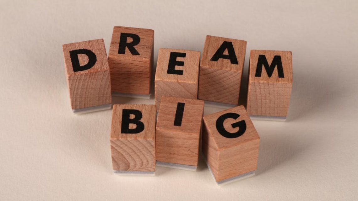 Inspiring arrangement of wooden blocks spelling 'Dream Big' on a neutral beige background.