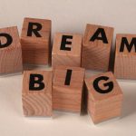 Inspiring arrangement of wooden blocks spelling 'Dream Big' on a neutral beige background.